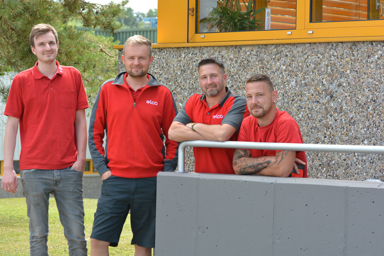 Four men in red T-shirts stand on a staircase